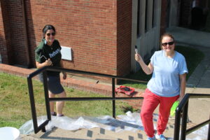 Two alumni standing with paint brushes 